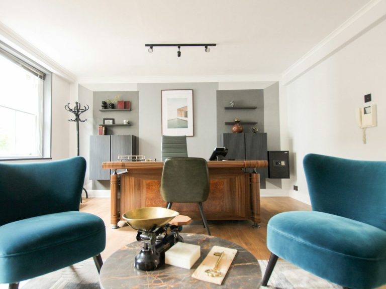 Oficina moderna con sillones turquesa y una mesa de madera en un ambiente luminoso.